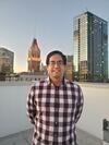 Photo of a man wearing glasses and a checkered shirt in front of the Oakland skyline