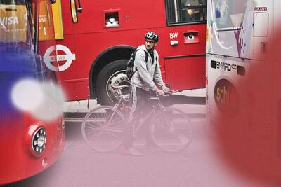 A man wearing a grey sweatshirt and black sweatpants rides a bicycle between three public transit buses